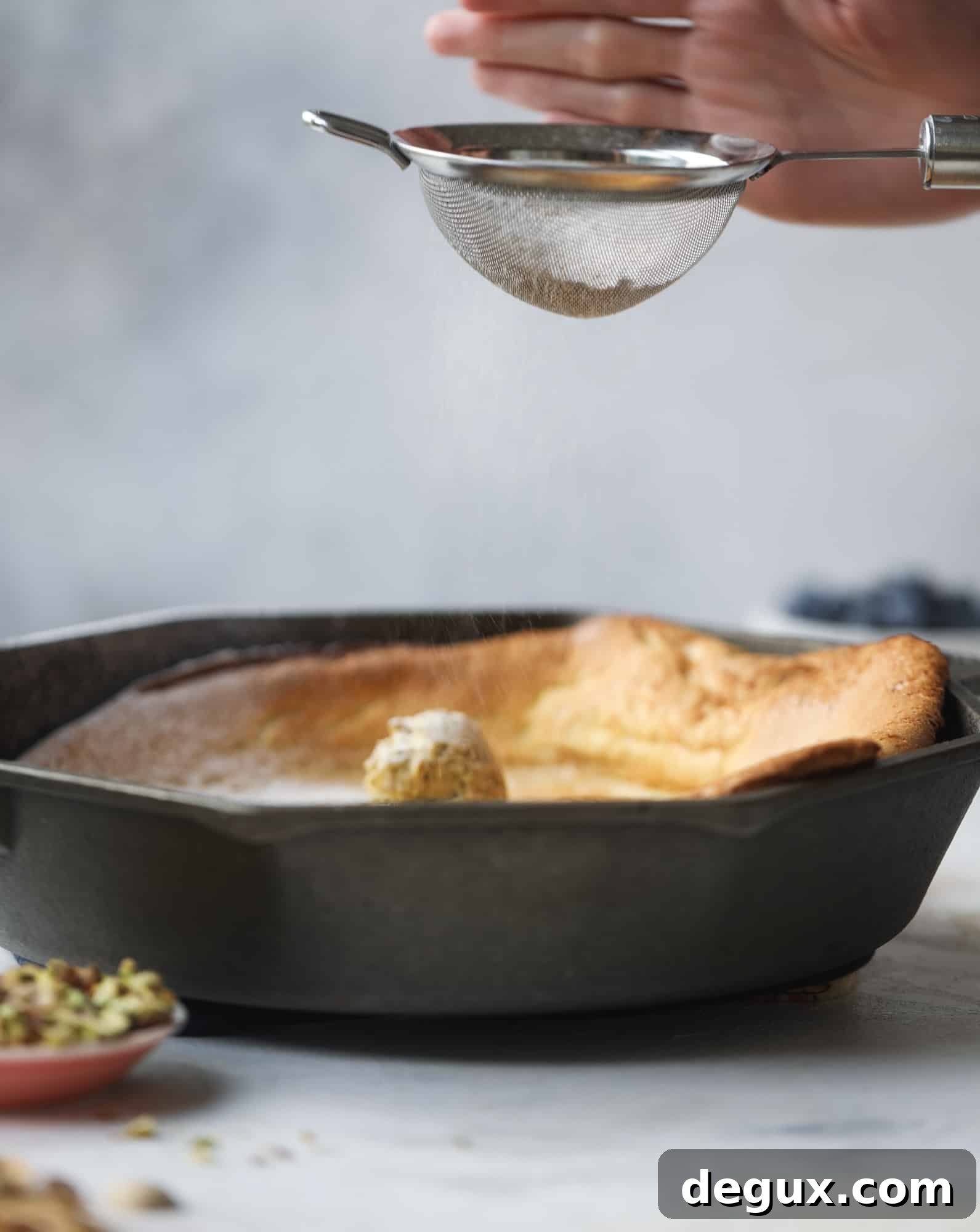 This incredible dutch baby recipe is fluffy and light and perfect for breakfast! It's sprinkled with pistachio sugar and served with pistachio butter and fresh blueberries.