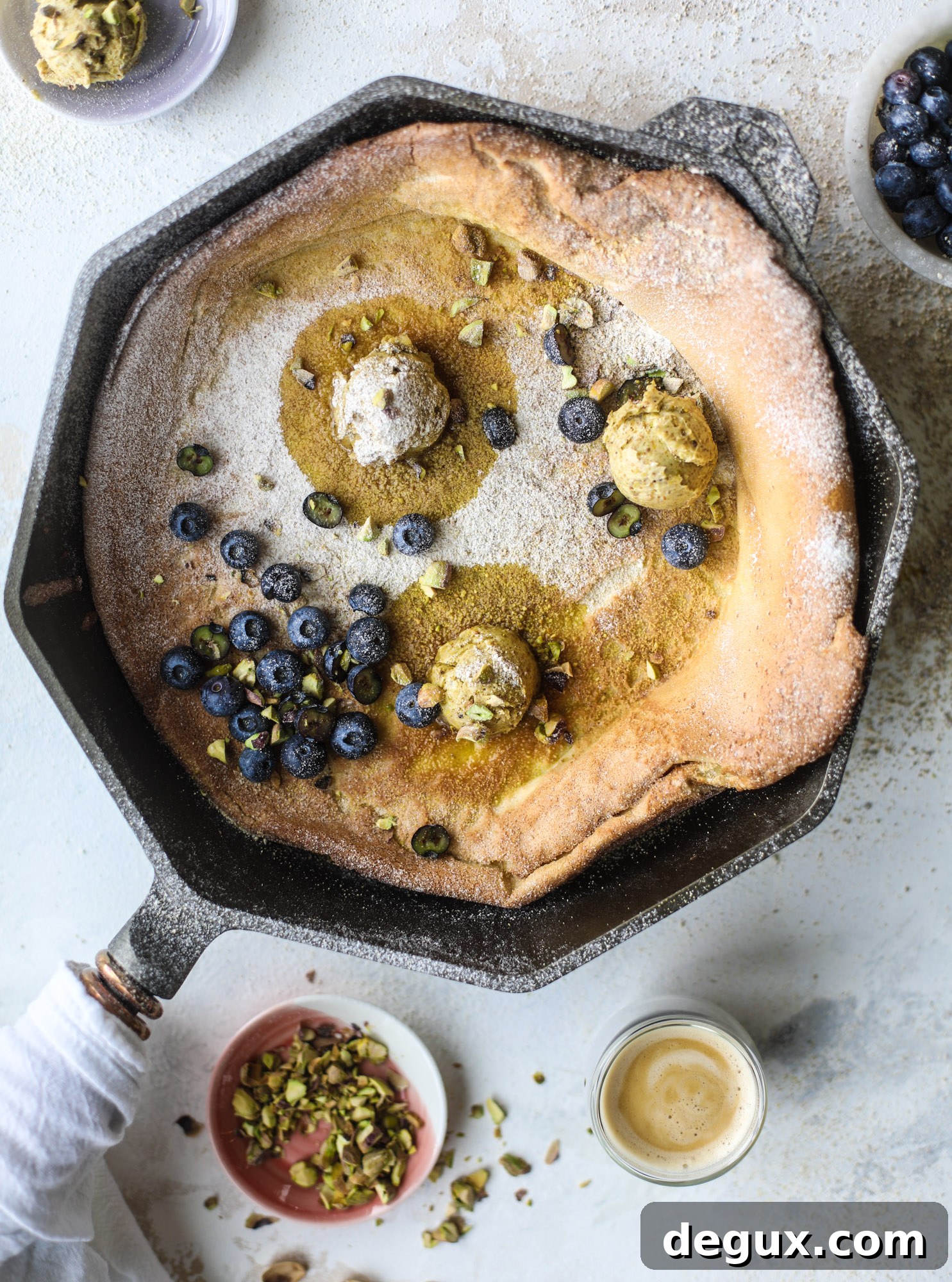 This incredible dutch baby recipe is fluffy and light and perfect for breakfast! It's sprinkled with pistachio sugar and served with pistachio butter and fresh blueberries.