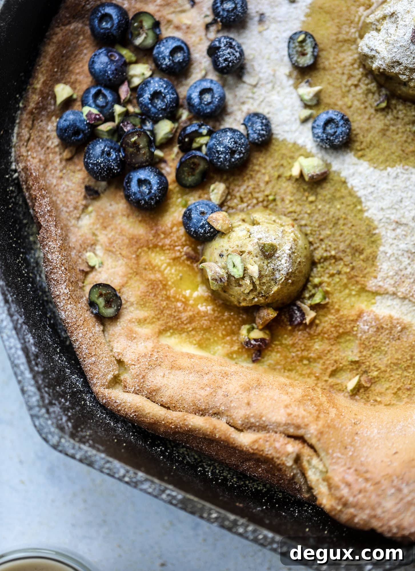 This incredible dutch baby recipe is fluffy and light and perfect for breakfast! It's sprinkled with pistachio sugar and served with pistachio butter and fresh blueberries.