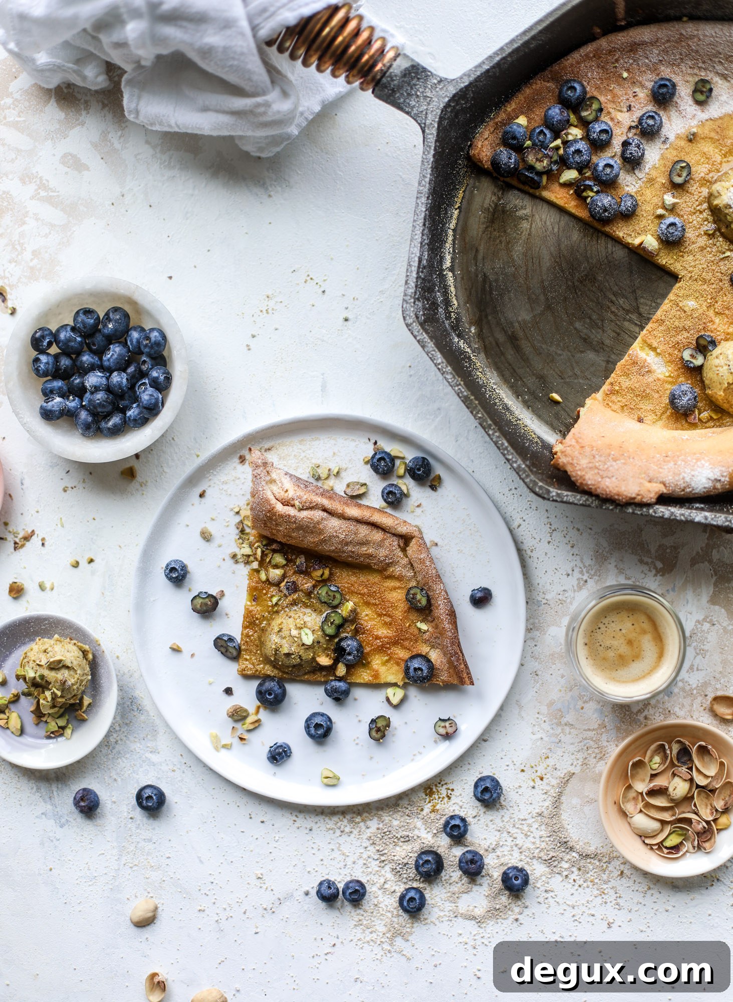 This incredible dutch baby recipe is fluffy and light and perfect for breakfast! It's sprinkled with pistachio sugar and served with pistachio butter and fresh blueberries.