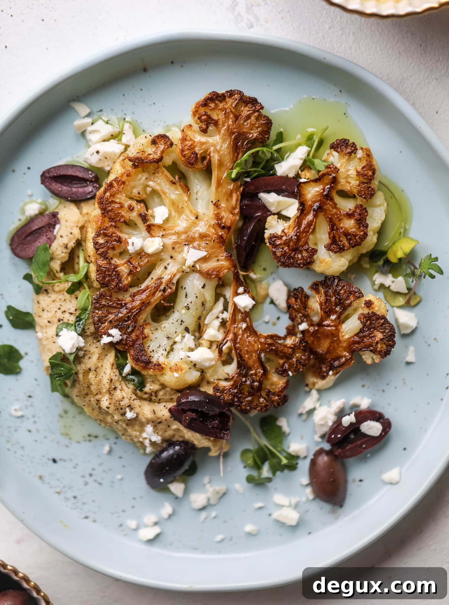 This roasted cauliflower with hummus, olives and feta is super flavorful and a wonderful meal, side dish or snack. Flavorful roasted cauliflower, creamy hummus, briney olives and tangy feta come together to make a major taste explosion. I howsweeteats.com #roasted #cauliflower #hummus #olives #feta