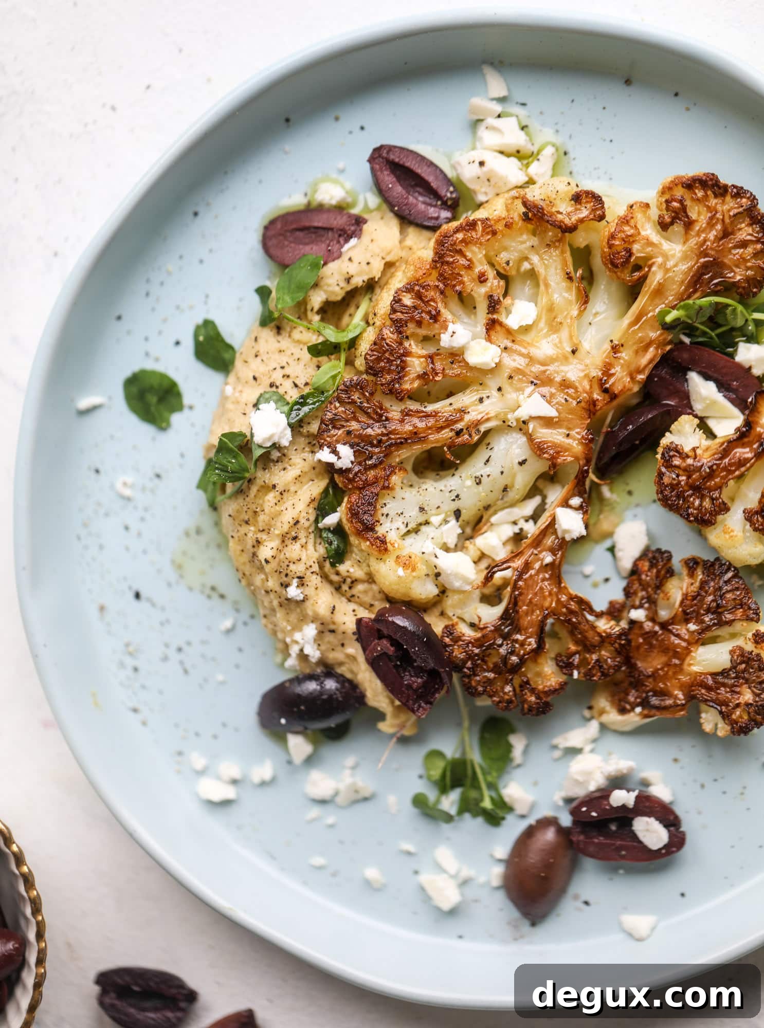 This roasted cauliflower with hummus, olives and feta is super flavorful and a wonderful meal, side dish or snack. Flavorful roasted cauliflower, creamy hummus, briney olives and tangy feta come together to make a major taste explosion. I howsweeteats.com #roasted #cauliflower #hummus #olives #feta