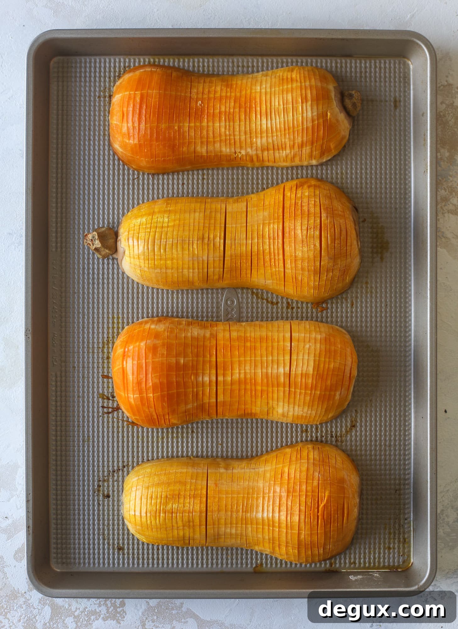Maple pecan and brown butter sage hasselback butternut squash on a baking sheet, ready for the oven.
