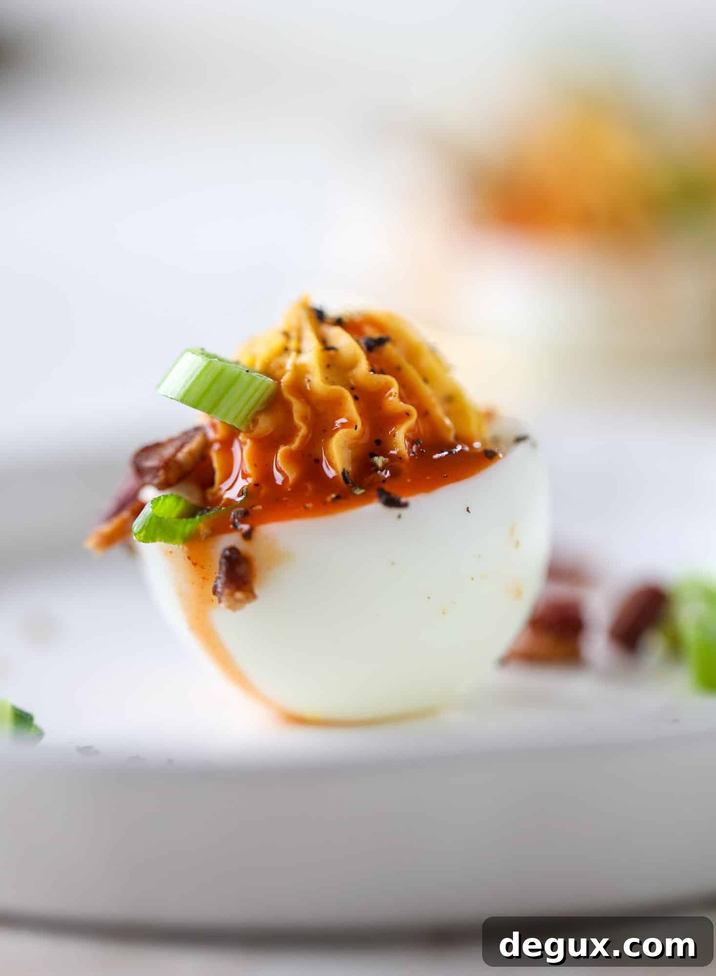 Buffalo deviled eggs are kicked-up deviled eggs! Made with goat cheese filling and served with buffalo wing sauce, crispy bacon and sliced scallions. I howsweeteats.com #deviledeggs #buffalo