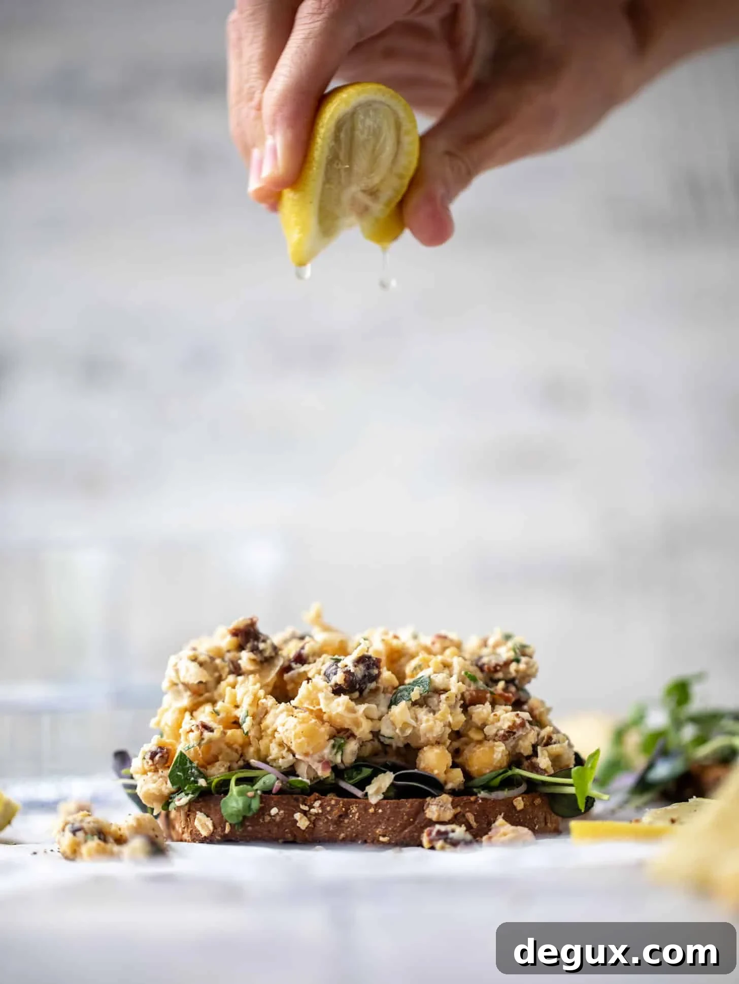 20-Minute Smashed Chickpea Salad for a Quick Flavorful Lunch 5 squeezing lemon on smashed chickpea salad on toast with micro greens