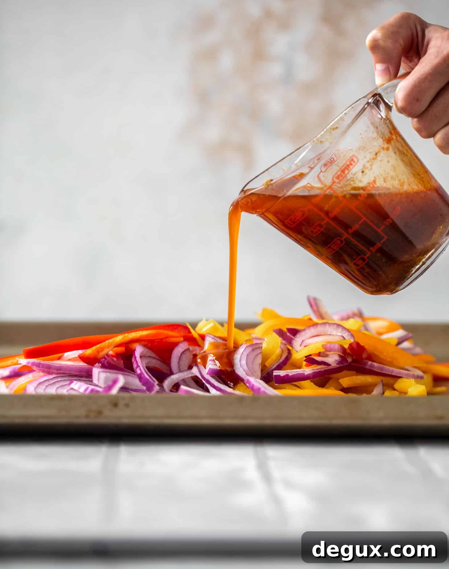 Lime Sheet-Pan Chicken Fajitas with Quick Guacamole 6 pouring fajita marinade on peppers and onions