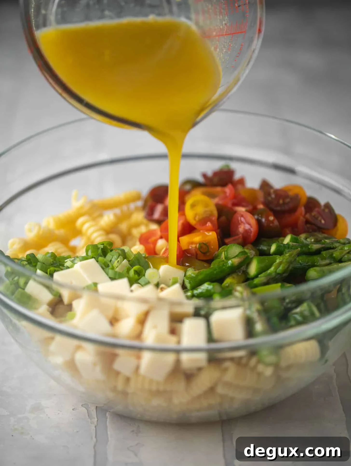 pouring honey mustard dressing on asparagus pasta salad