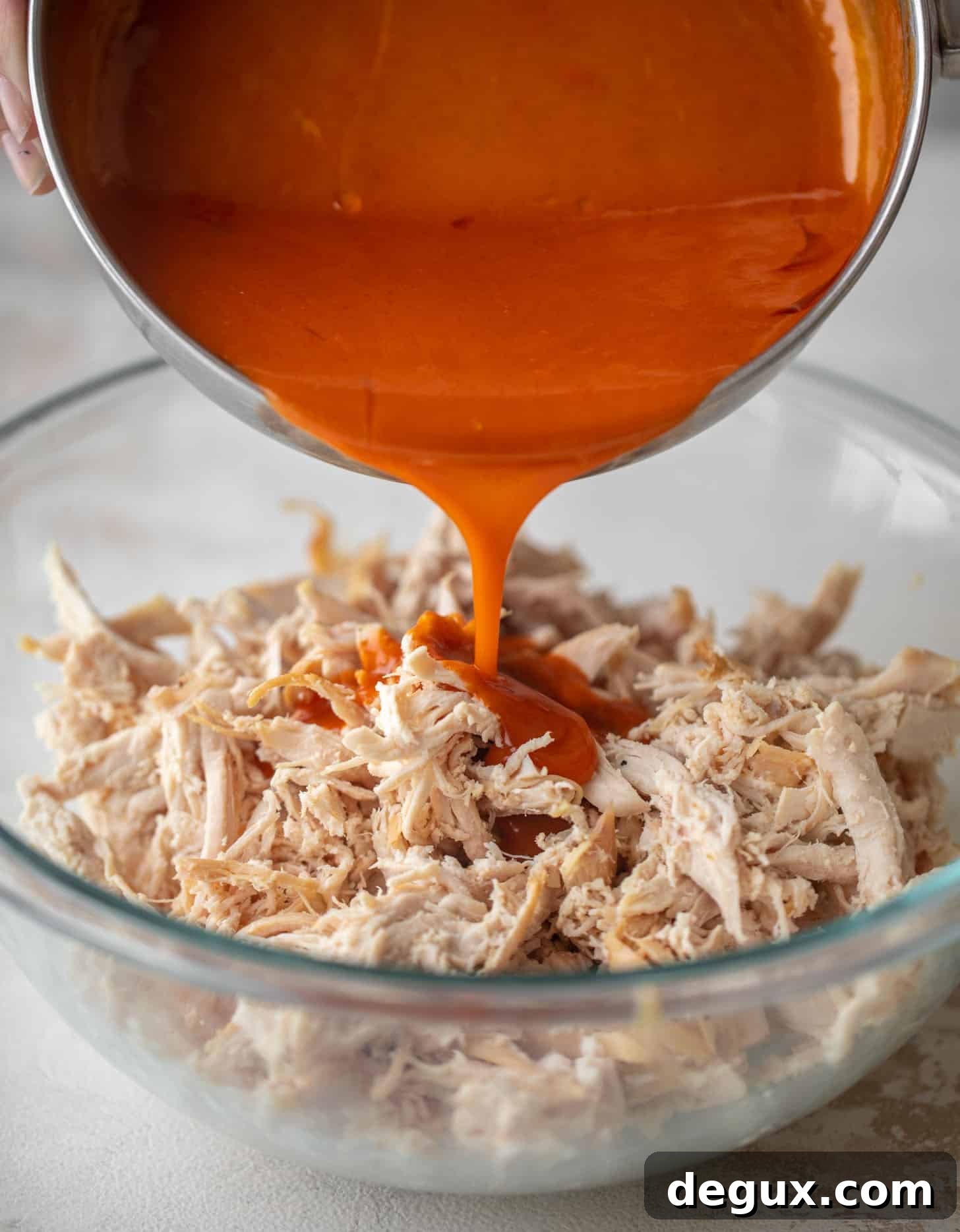 Buffalo Chicken Pull-Apart Sliders with Gorgonzola Slaw 3 pouring buffalo wing sauce on shredded chicken