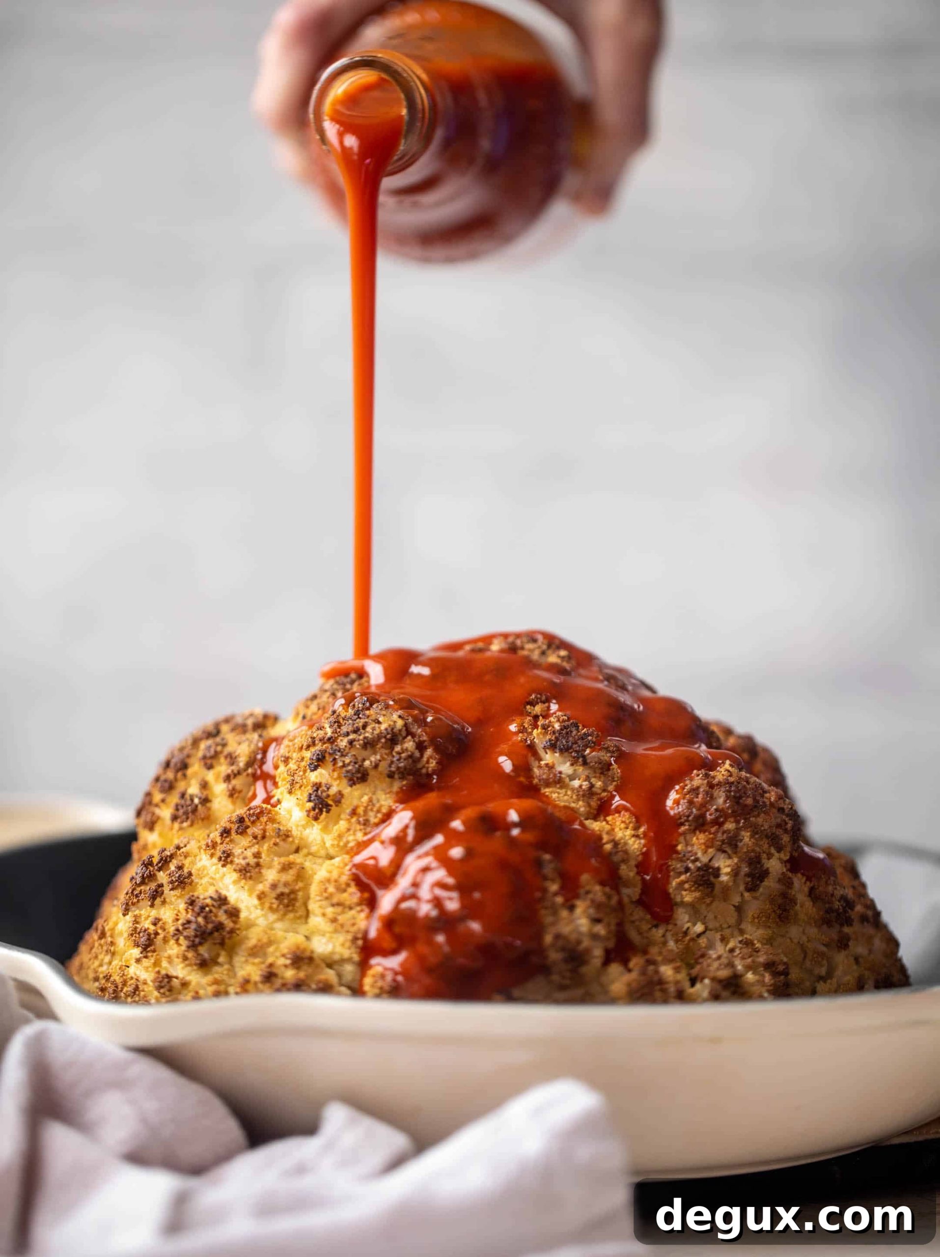 pouring buffalo sauce on whole cauliflower